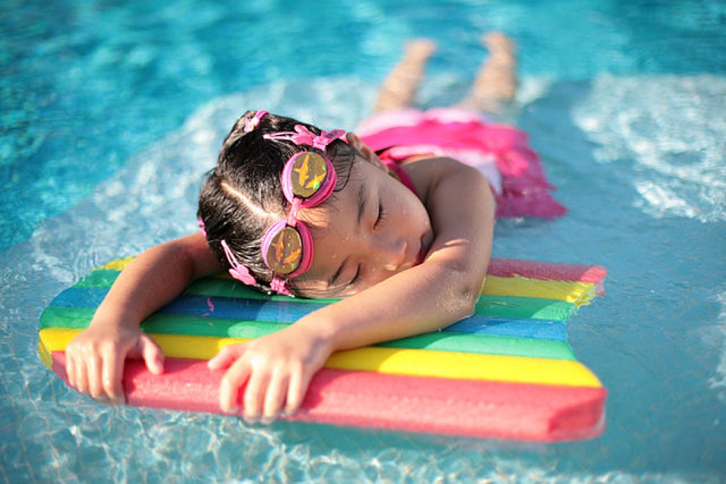 a little girl rests in a pool on a rainbow-colored swimming board